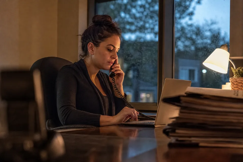 Intake coordinator taking a new client call at a law office front desk in the evening